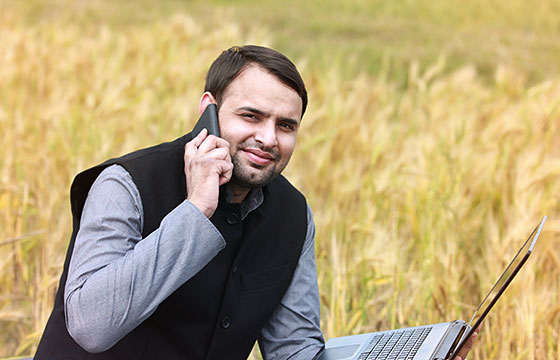 Man in a field with a phone and laptop computer.